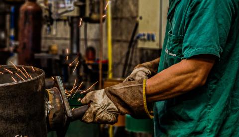 Welder wearing protective gear sparks metal in an industrial setting, showcasing skilled craftsmanship.