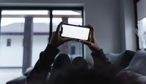 Person holding a smartphone while relaxing on the couch at home, blank screen.
