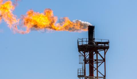 Close-up of an industrial gas flare with a vibrant orange flame against a clear blue sky.