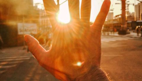A hand reaching towards the sun during a beautiful sunset on a city street.