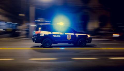 Blurred motion capture of a police car speeding at night with flashing lights on a city street.