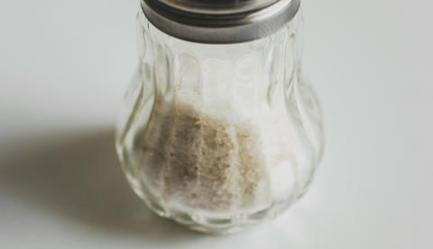 Minimalist photo of a glass salt shaker on a plain white background.