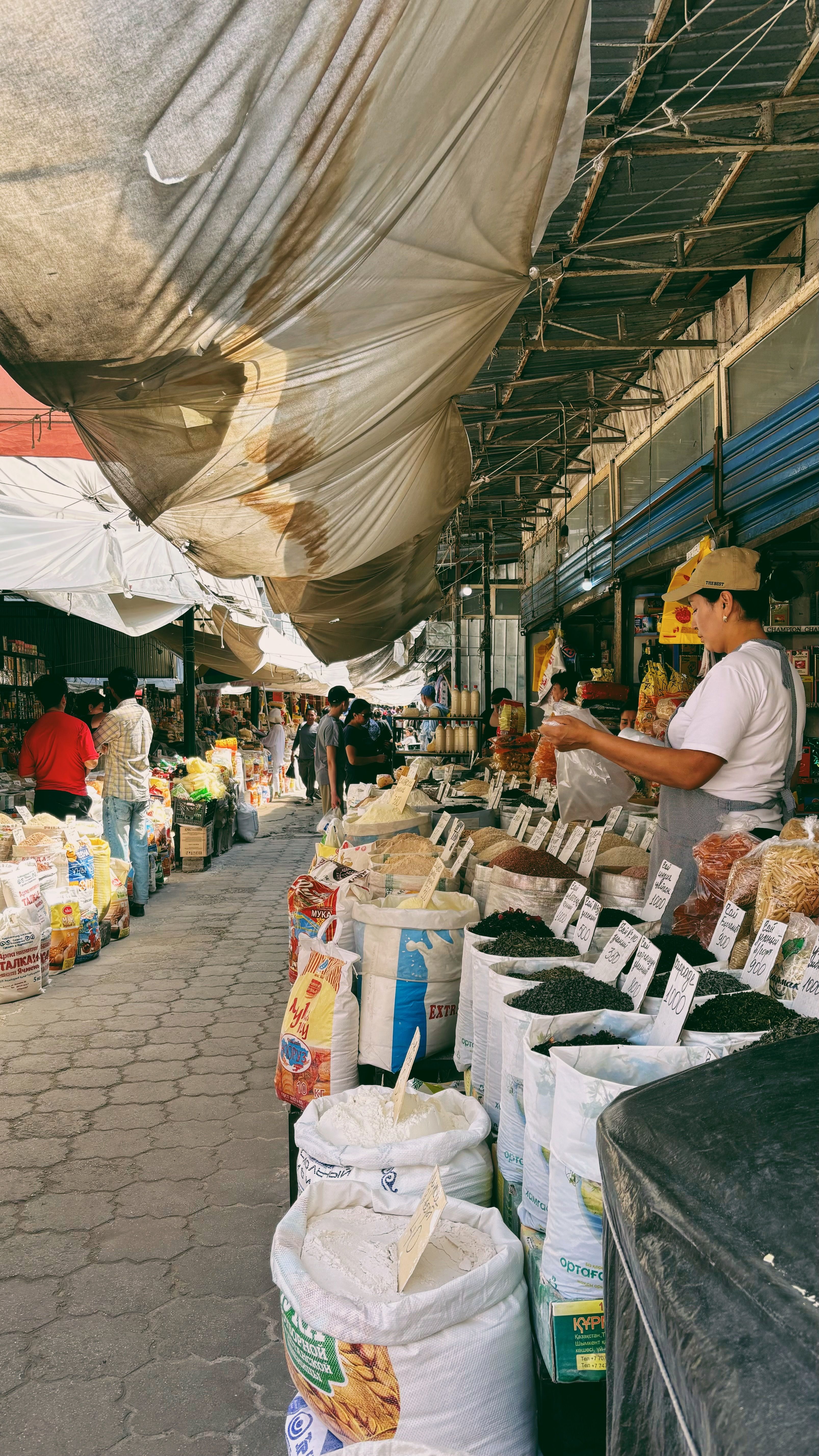 Busy market scene with various vendors selling goods outdoors under canopies.