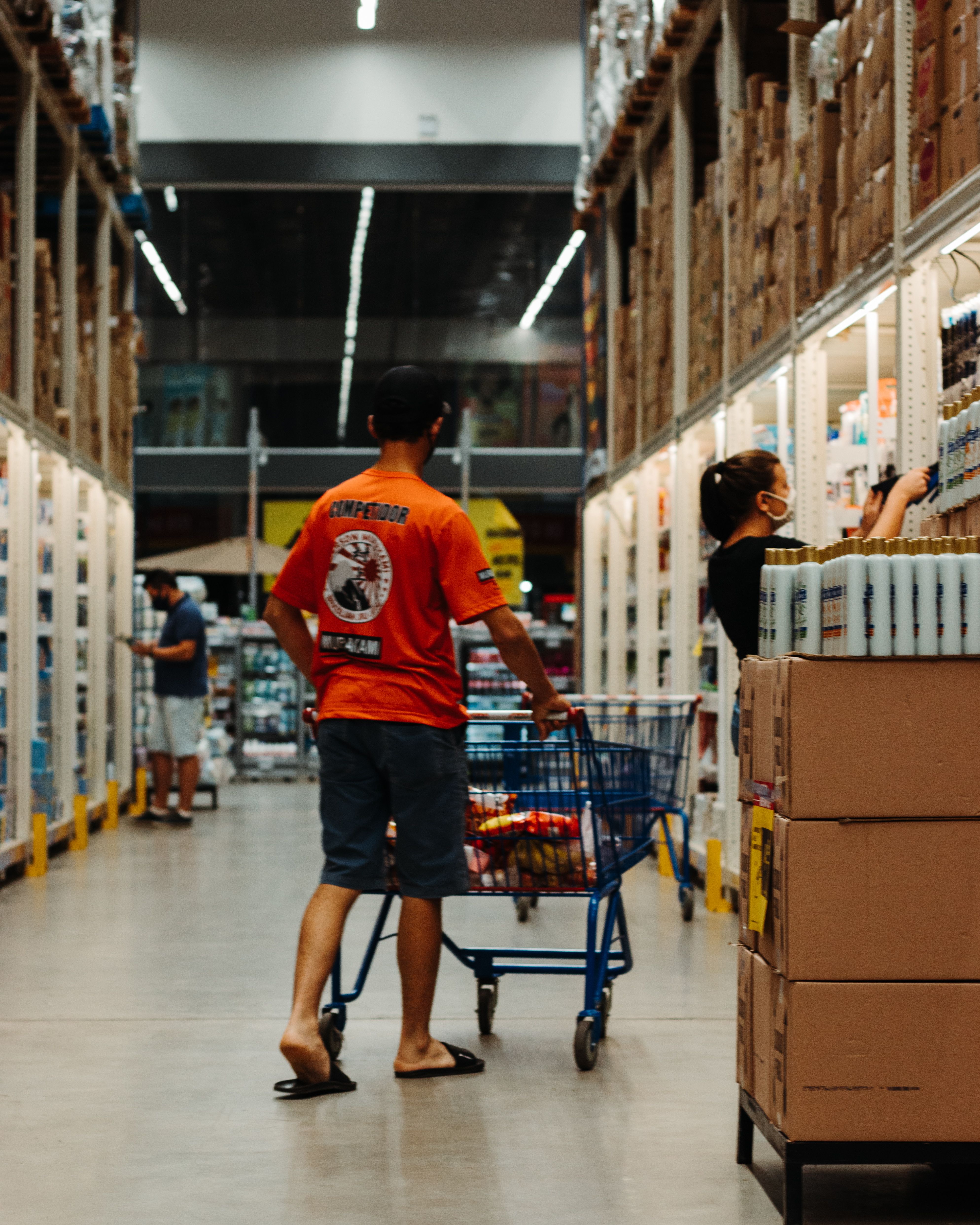 Shoppers explore a supermarket aisle filled with various products and full carts, highlighting everyday grocery shopping.